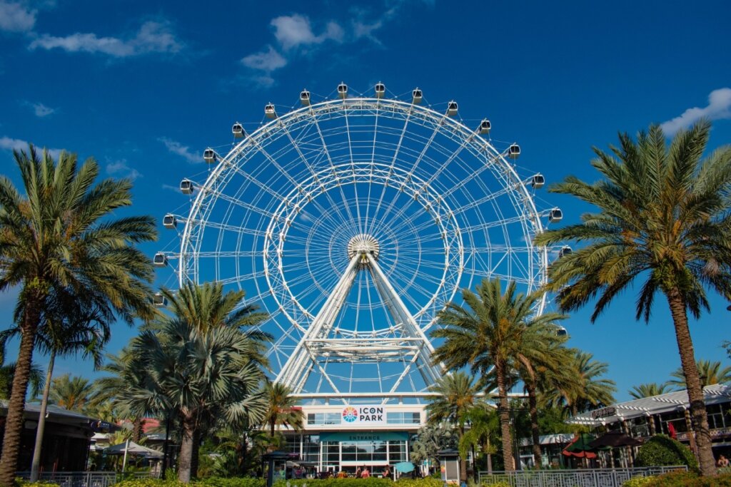 Imagem de uma roda gigante em Orlando com céu azul de fundo e árvores na frente