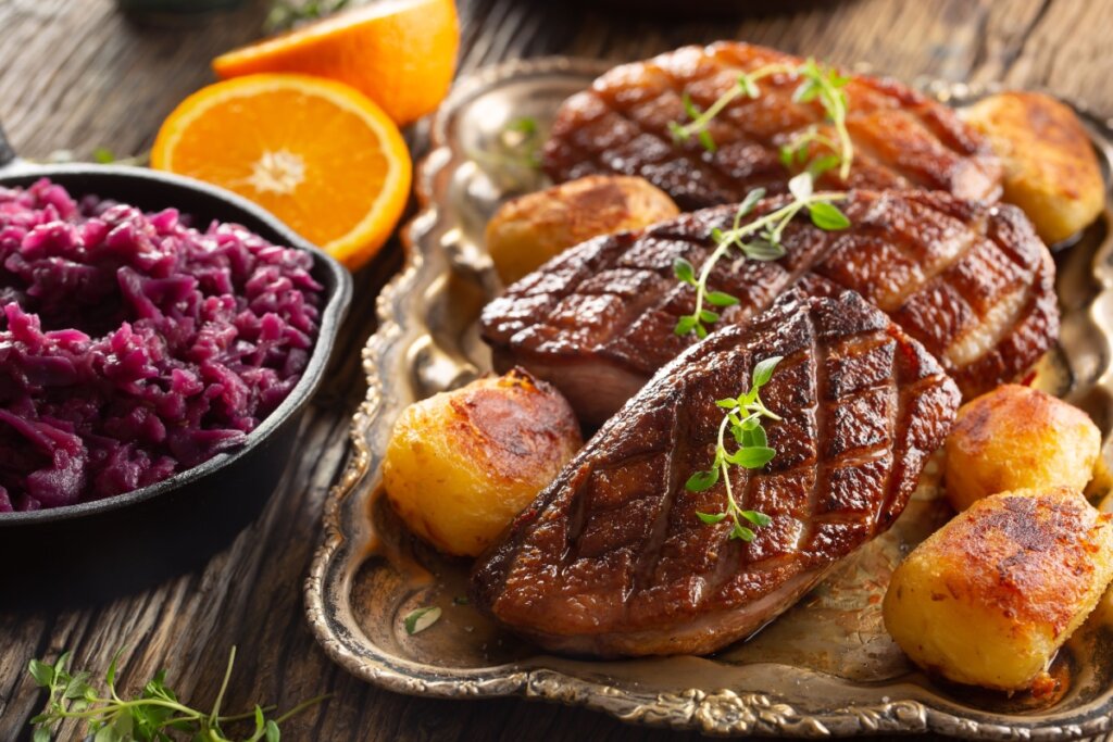 Peito de pato grelhado com batatas assadas e repolho roxo; laranjas cortadas ao redor