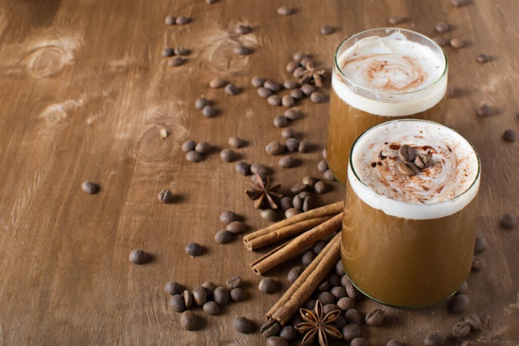 Shake de café com aveia e whey em dois copos; grãos de café e paus de panela ao redor