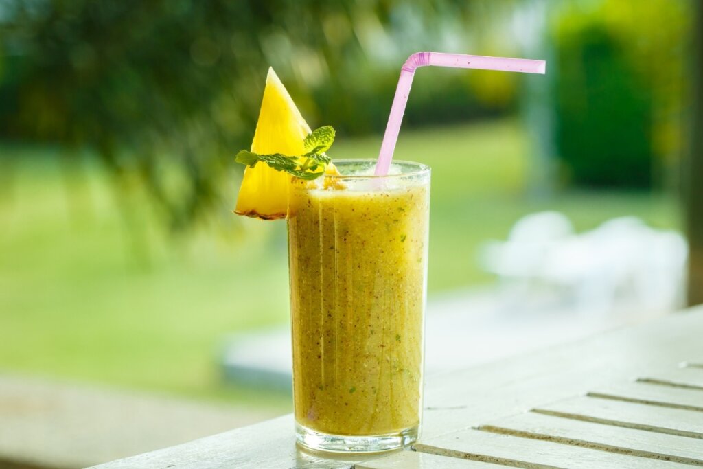 Copo de vidro com suco de abacaxi com hortelã decorado com uma fatia de abacaxi e folhas de hortelã