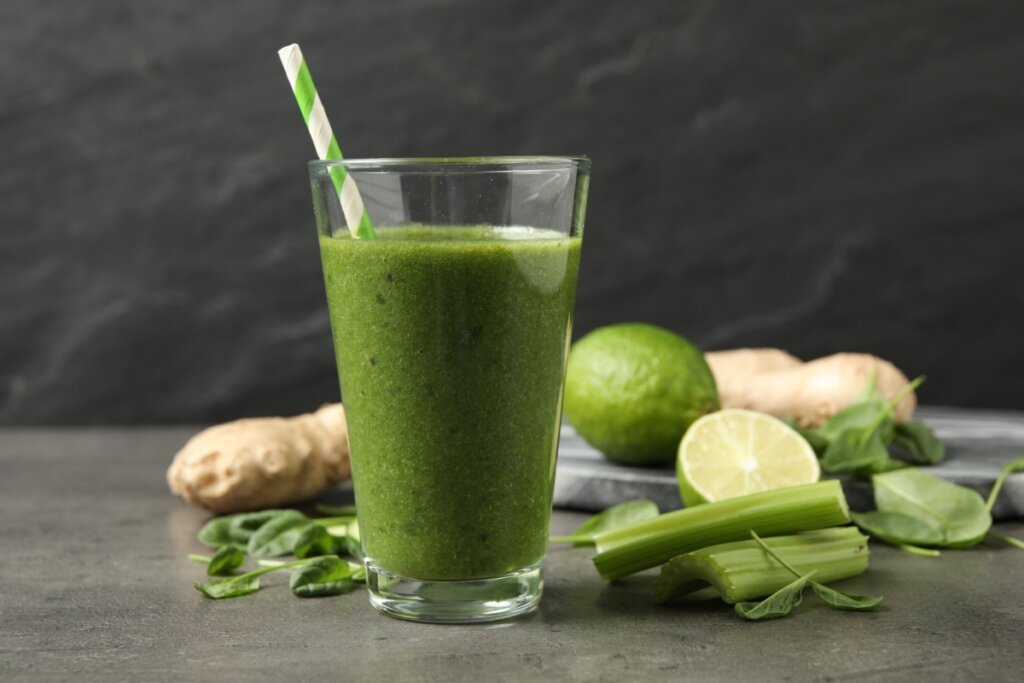 Suco verde em um copo de vidro com folhas de espinafre, rodelas de limão e pedaços de gengibre ao redor