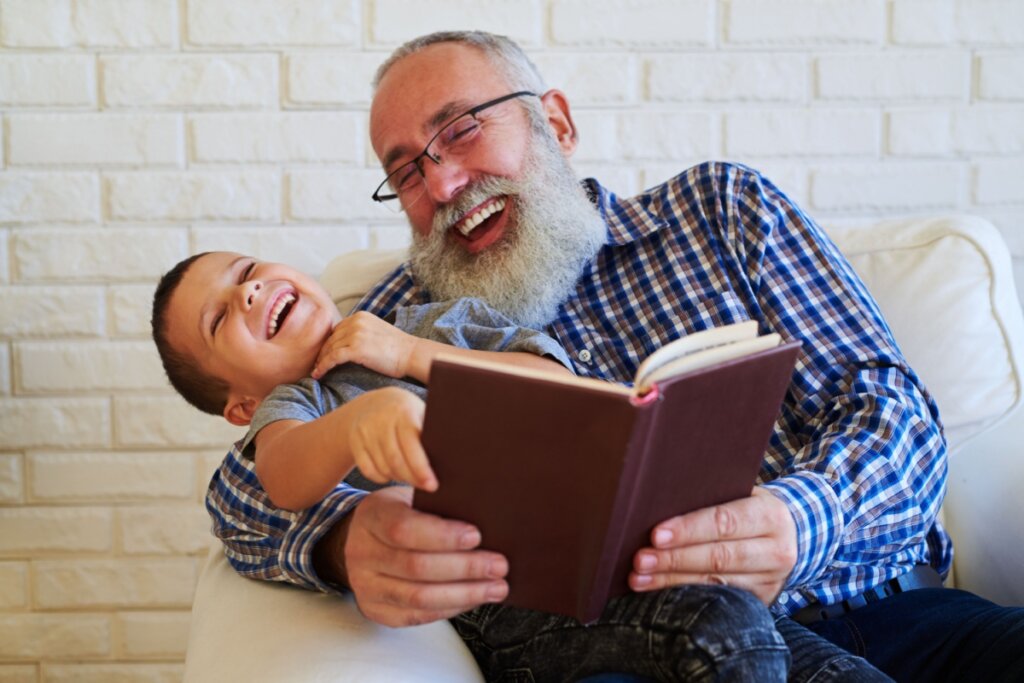 Avô sentado com o neto no colo lendo um livro juntos e rindo