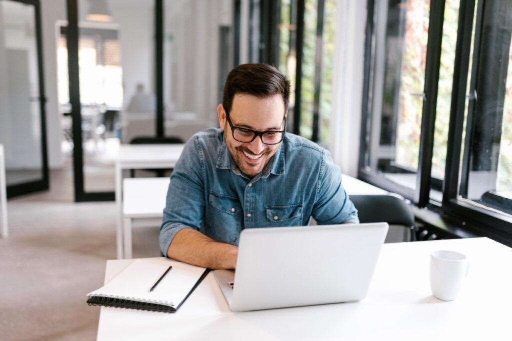 Homem sorrindo usando notebook em sala comercial