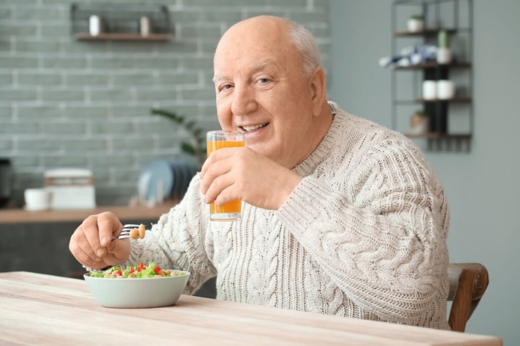 idoso sentado à mesa comendo salada e bebendo suco