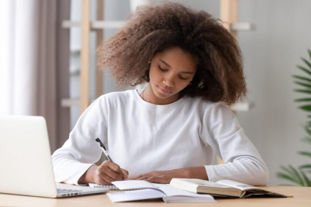 menina jovem sentada escrevendo em mesa com livros e notebook