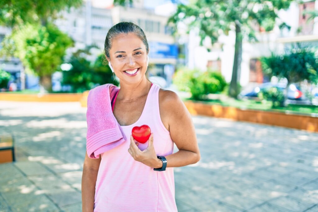 mulher com roupa rosa, toalha rosa no ombro e segurando coração vermelho perto do peito