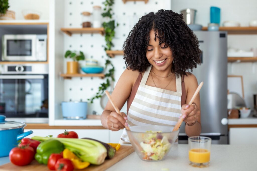 mulher de avental na cozinha mexendo salada em recipiente com duas colheres