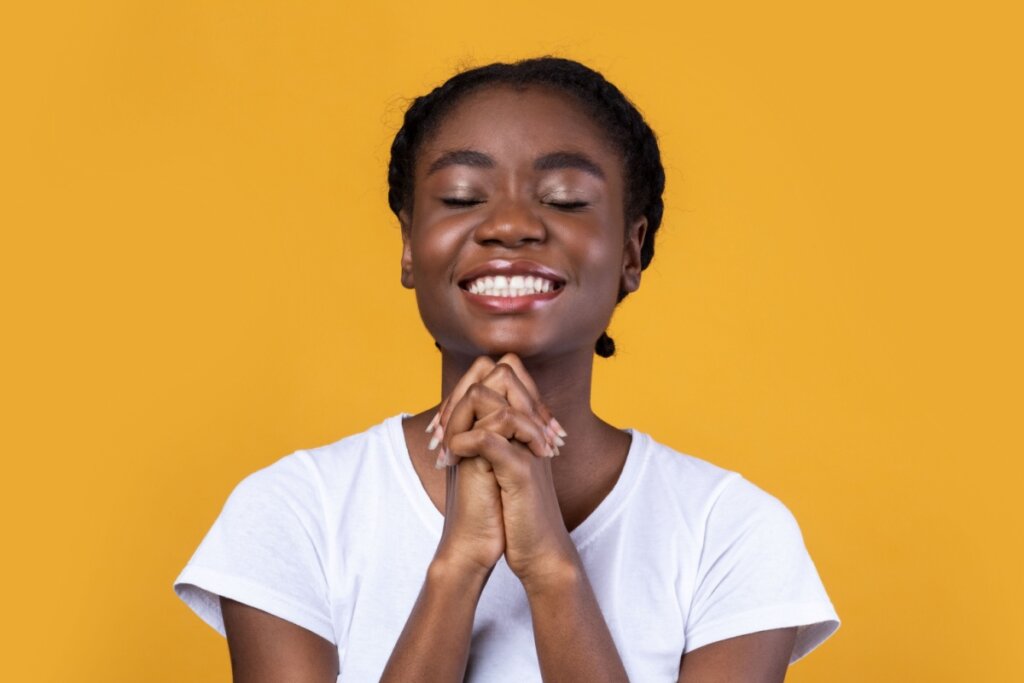 mulher sorrindo rezando em fundo amarelo