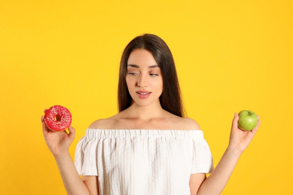 Mulher segurando em uma mão, um donut e na outra uma maçã