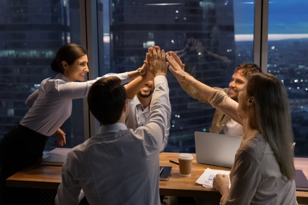 cinco pessoas em torno de mesa de trabalho com as mãos unidas