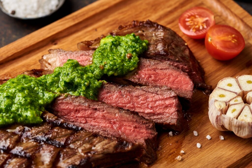 Picanha fatiada servida com chimichurri em tábua de madeira