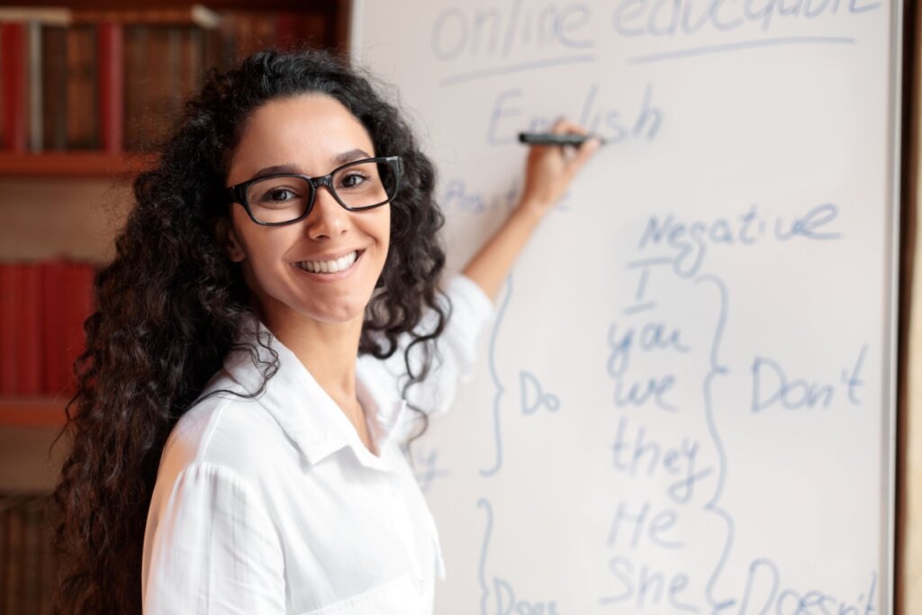 mulher de camisa branca e óculos pretos escrevendo em inglês em quadro branco