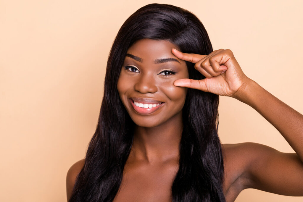 Mulher negra sorrindo com mão na sobrancelha