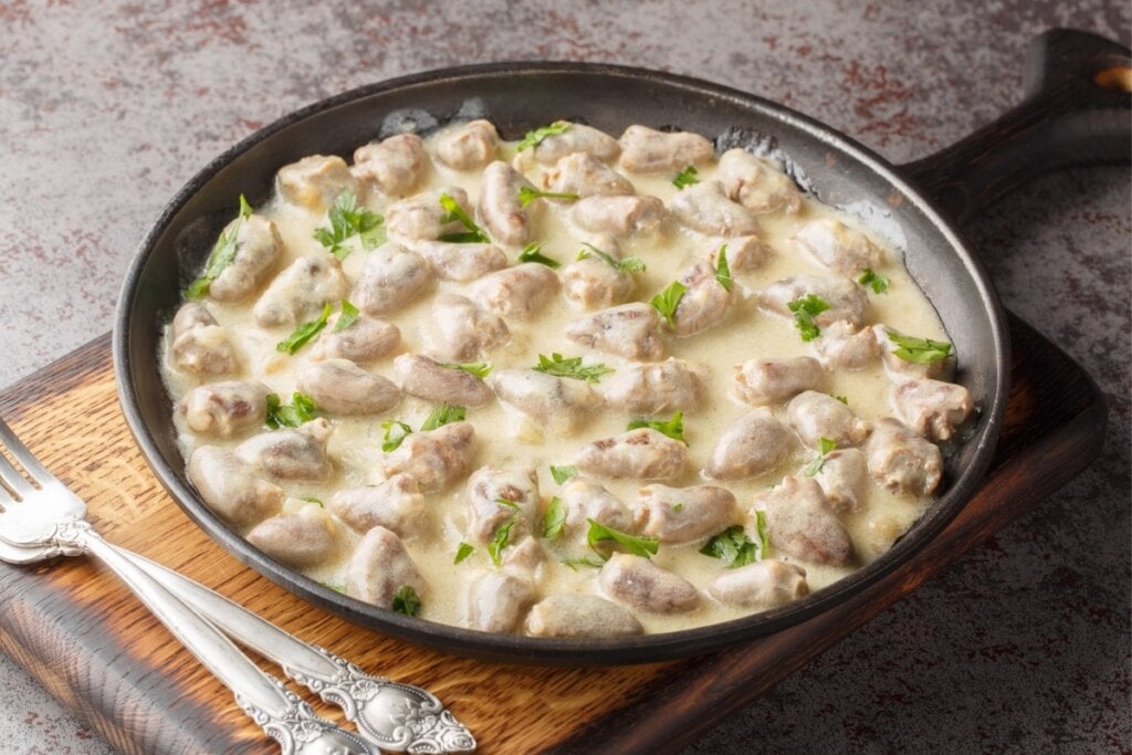 Frigideira preta com coração de frango, molho branco e salsinha picada