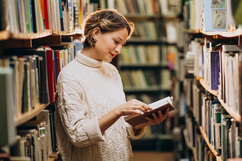 Mulher em pé em uma biblioteca lendo um livro