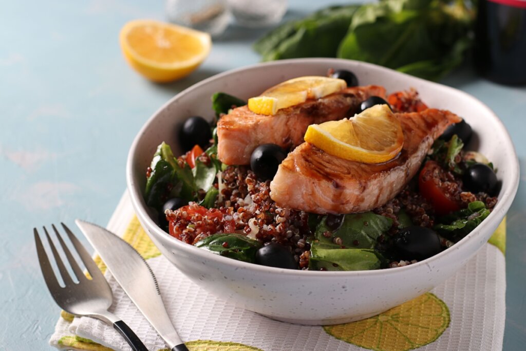 Salada de quinoa com salmão grelhado, espinafre, azeitonas, tomates-cereja e limão em recipiente branco