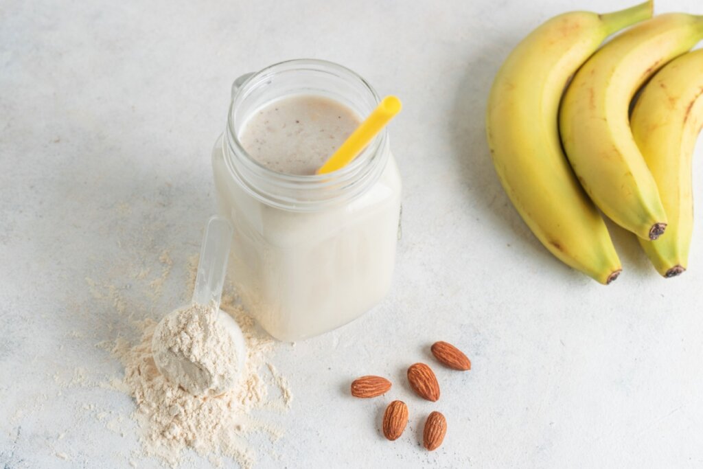 copo de vidro com vitamina e banana e amêndoas ao lado