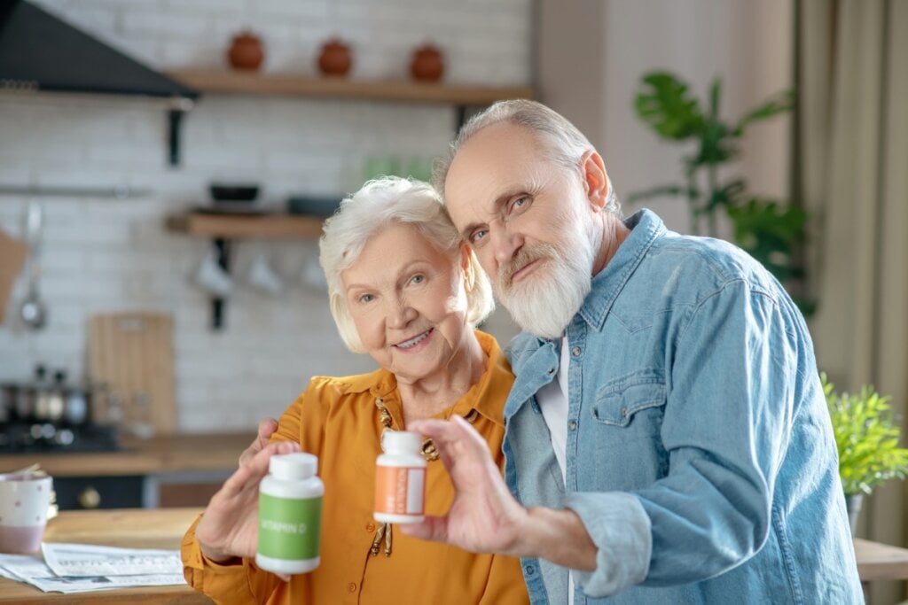 Casal de idosos abraçados segurando dois potes de suplementos