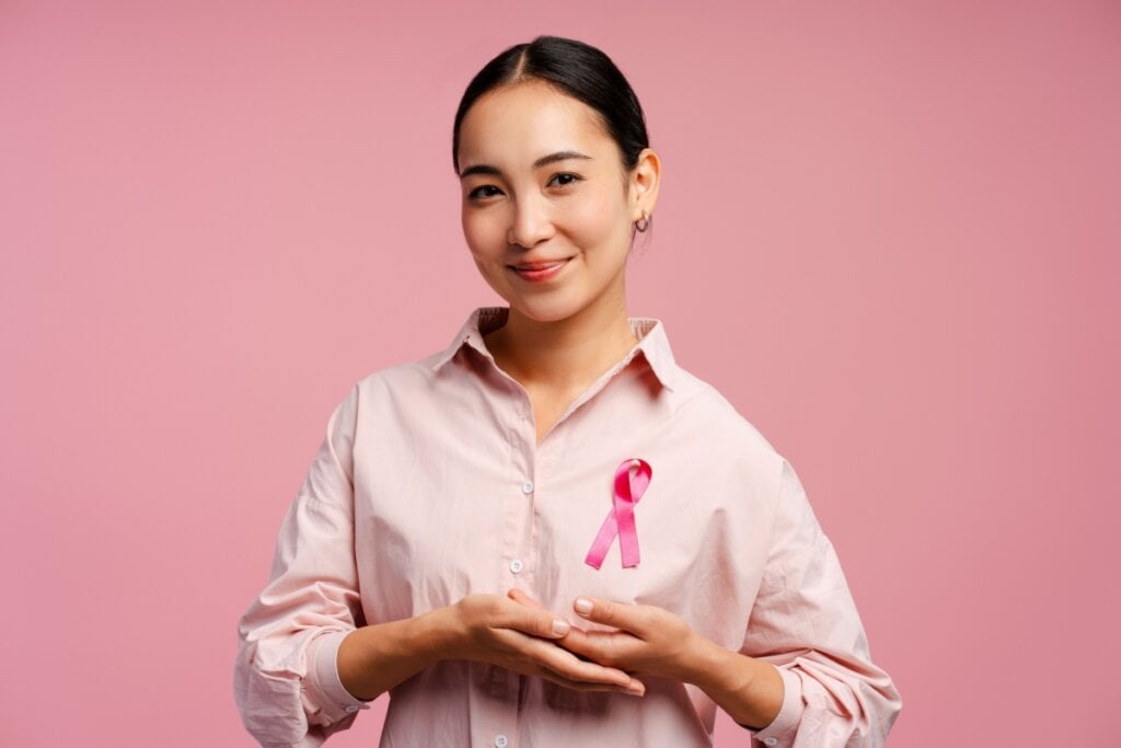 mulher sorrindo com mãos próximas ao seio e com laço rosa