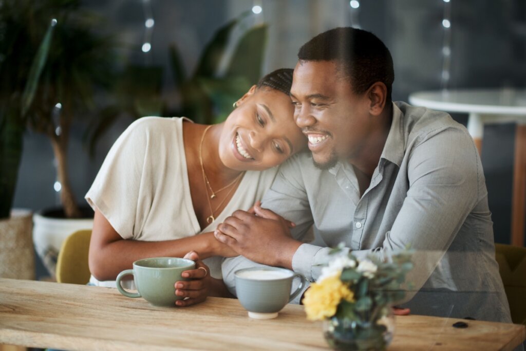 Casal sorridente aproveitando um momento de qualidade juntos, sentados em uma mesa com xícaras de café