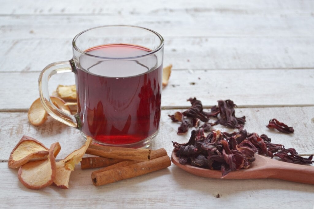 caneca de vidro com chá de hibisco. hibisco, canela e maçã desidratada em volta