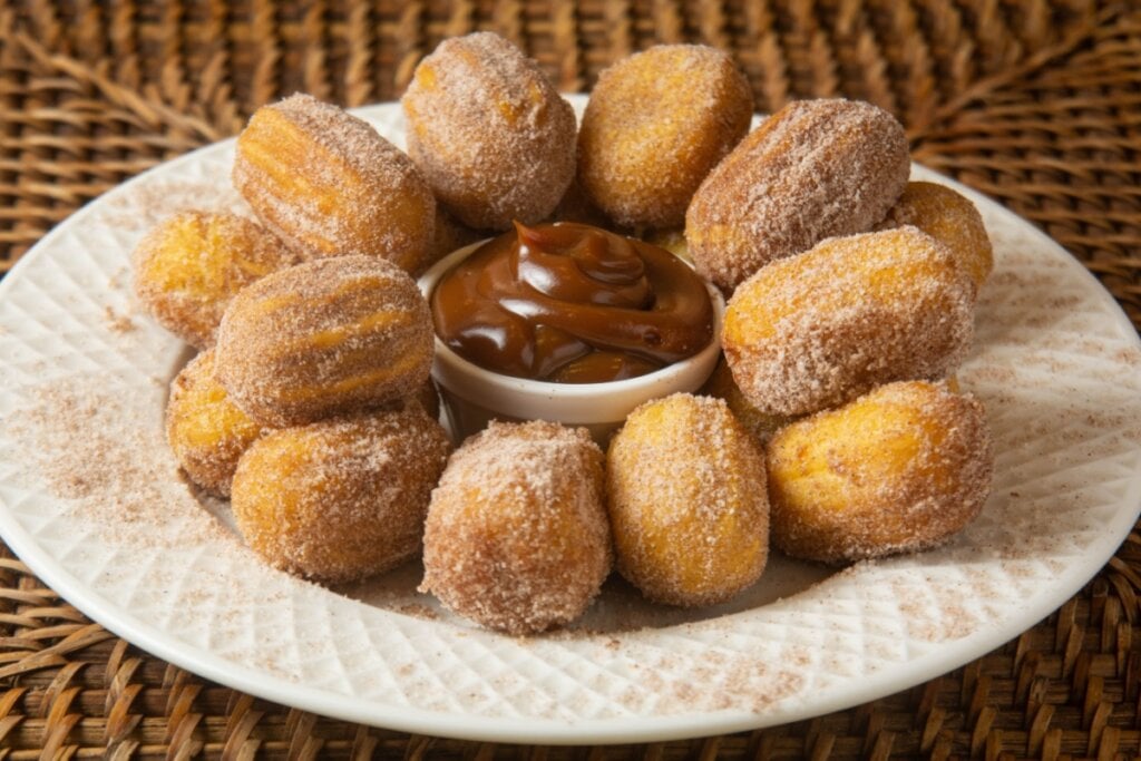 Churros servido em prato branco com um pote de doce de leite