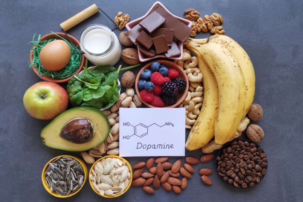 Imagem de alimentos ricos em nutrientes, como frutas, nozes e chocolate, organizados ao redor de um cartão com a fórmula química da dopamina