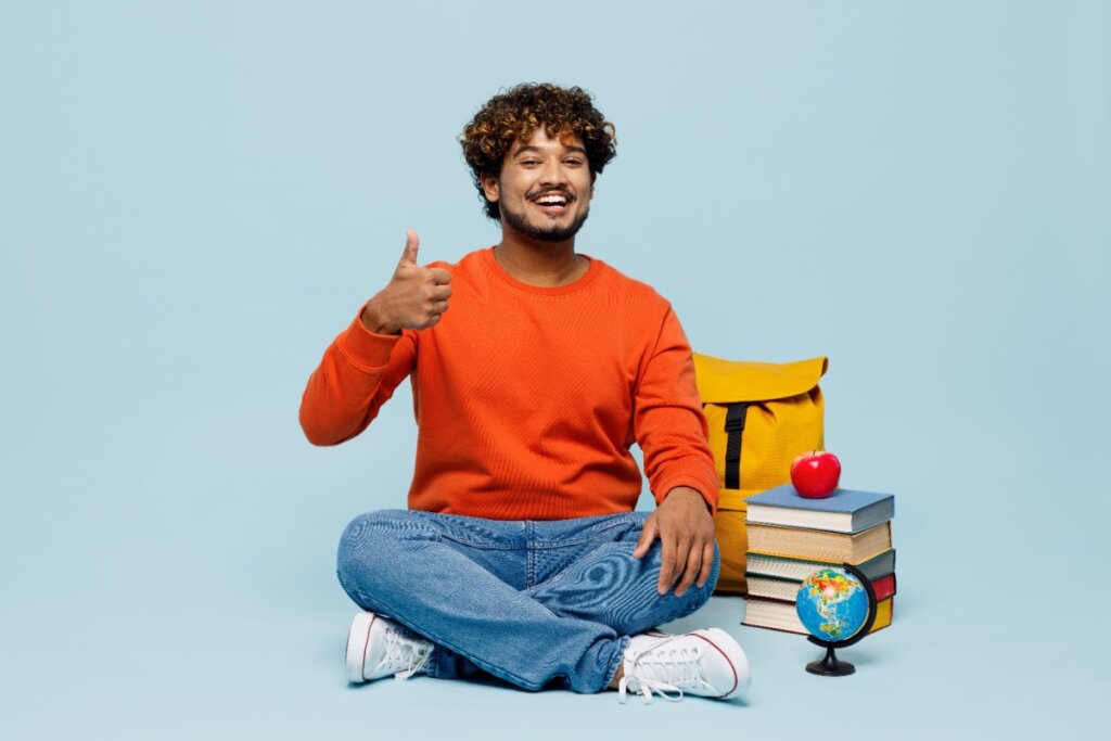 Estudante sorridente sentado com mochila, maçã, livros e globo ao lado