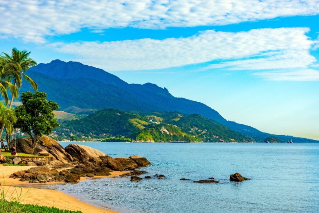 Paisagem de Ilhabela com uma praia de areia clara, pedras e vegetação tropical