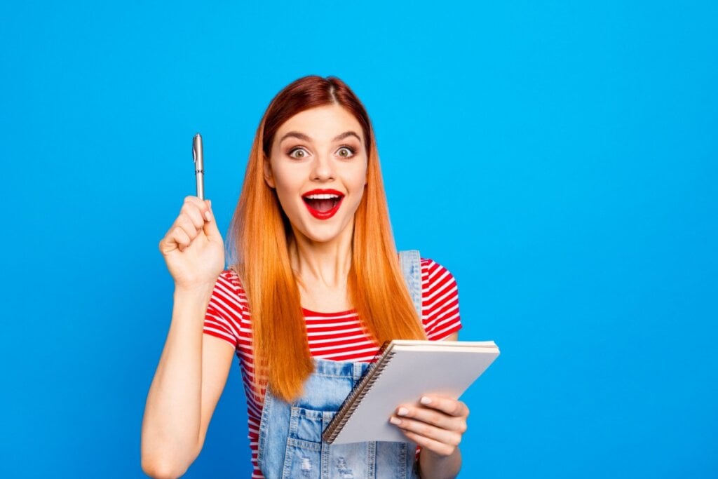 menina com cara de surpresa apontado caneta para cima e segurando caderno