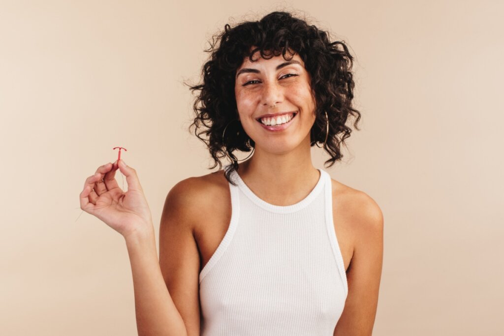 Jovem sorrindo segurando um DIU em uma mão