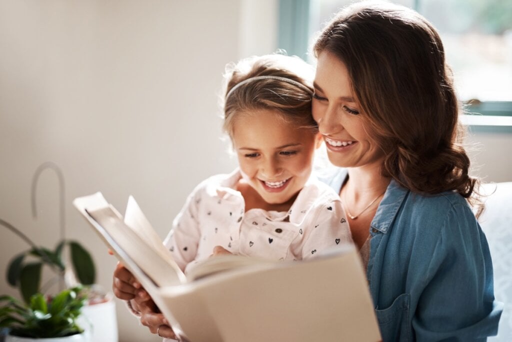 Mãe lendo livro com filha; ambas sorridentes