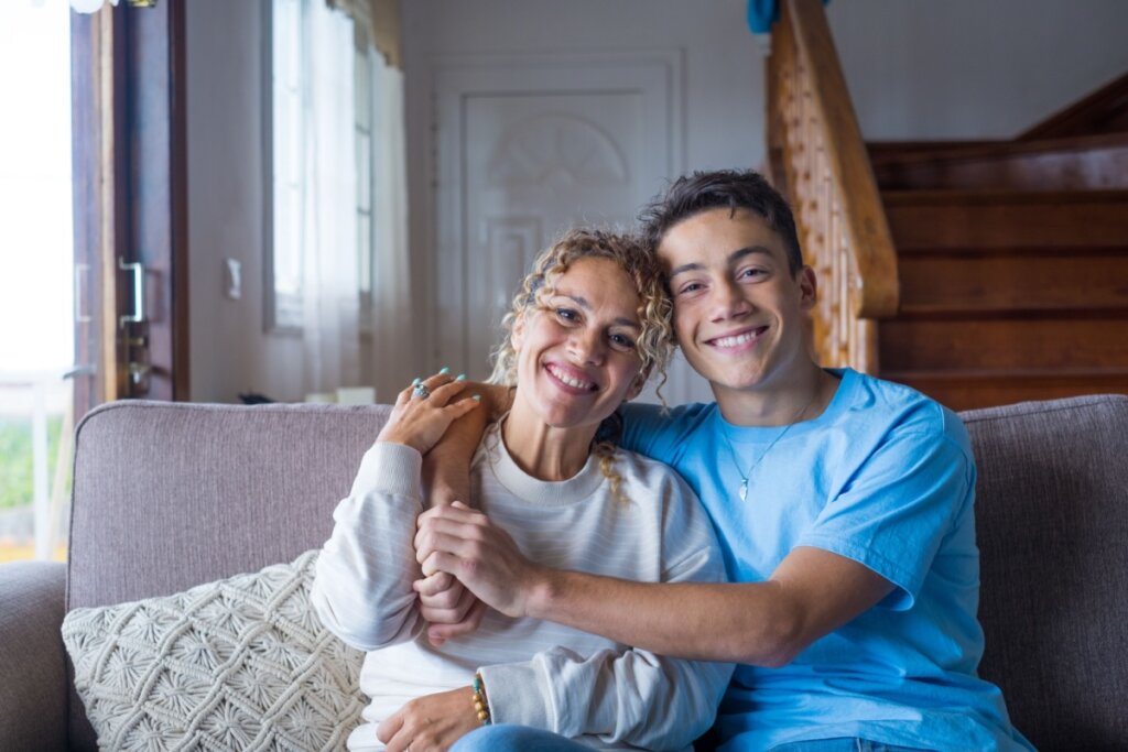 Mãe e filho sentados abraçados no sofá com uma expressão feliz