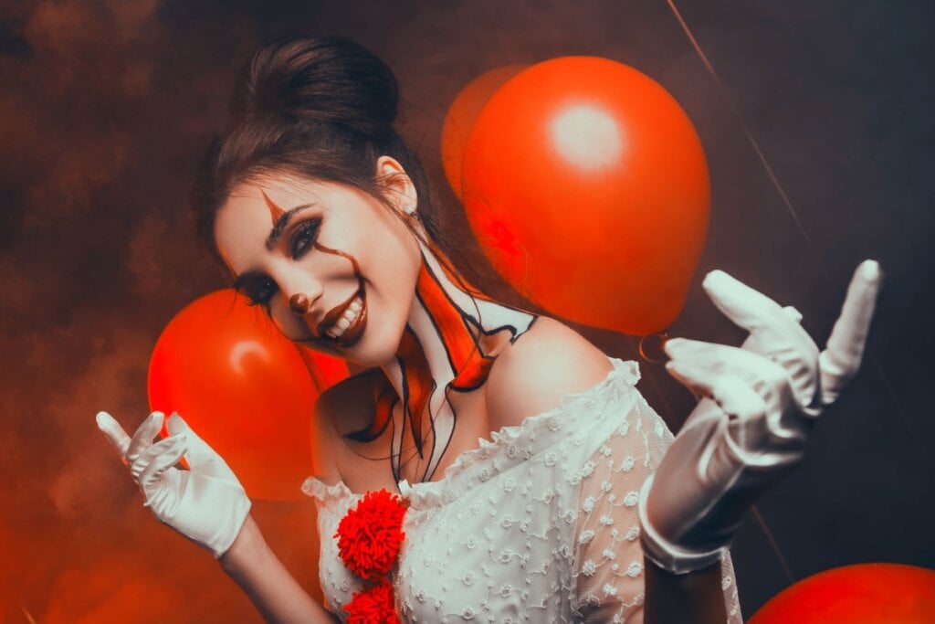 mulher sorrindo com maquiagem e roupa de palhaço de halloween e balões vermelhos ao fundo