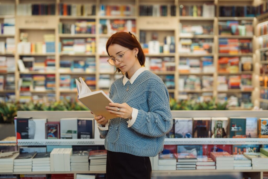 mulher de blusa cinza lendo livro em livraria