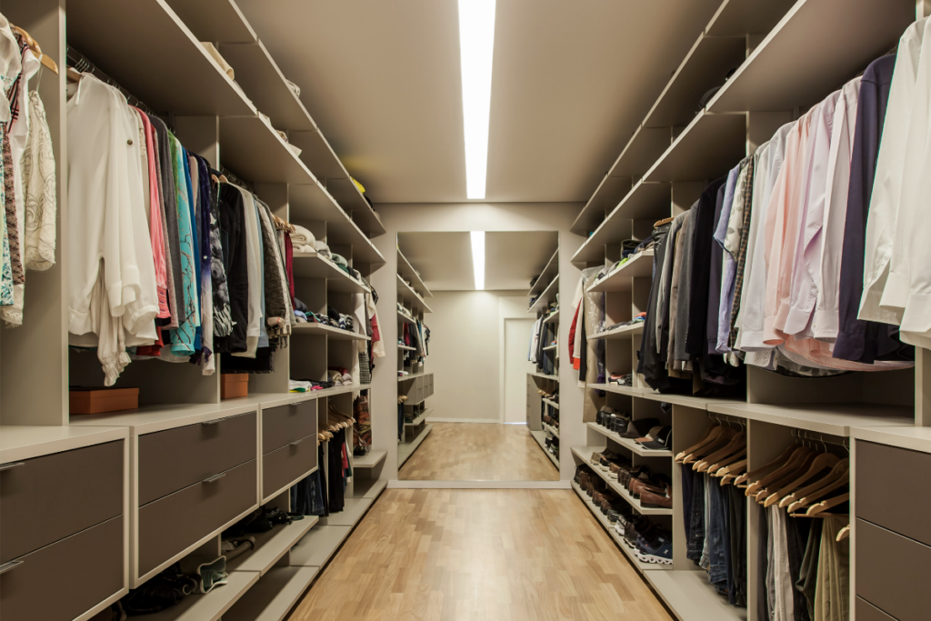 Closet com nichos e locais com roupas dos dois lados e no fim do espaço um espelho de corpo inteiro