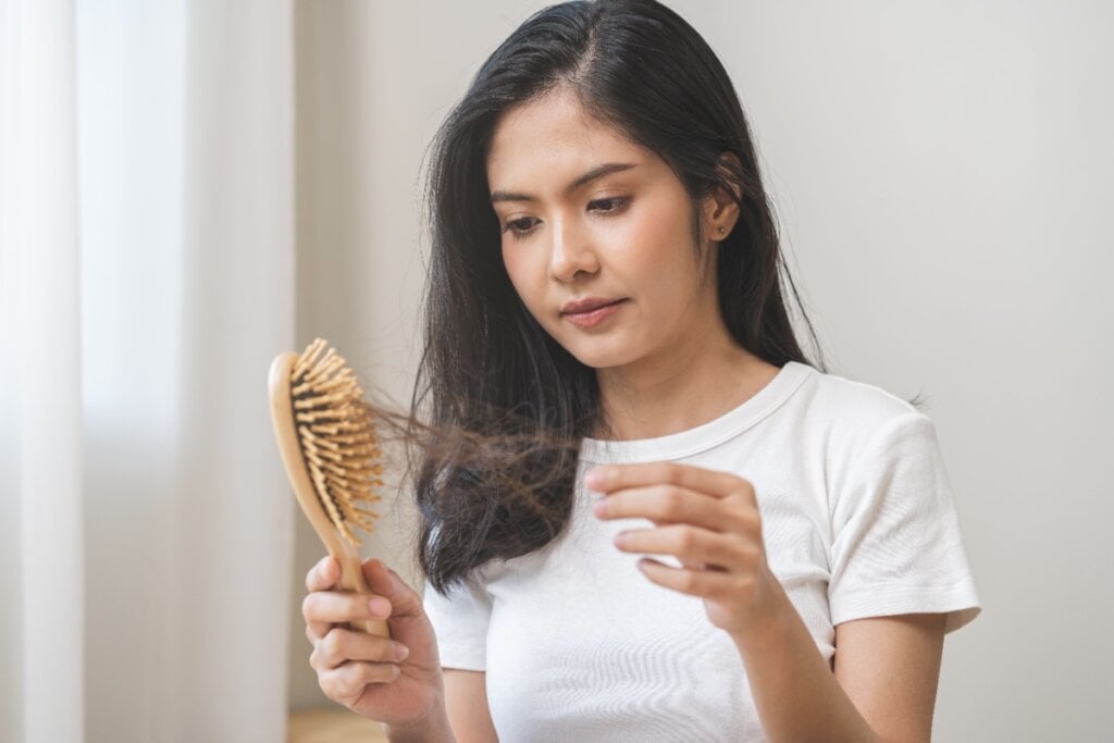 Mulher segurando escova com fios de cabelo caídos de sua cabeça