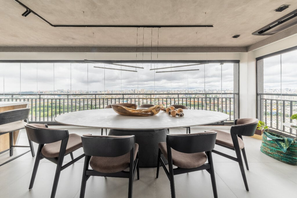 Varanda com mesa de cimento queimado e cadeiras cinzas ao redor