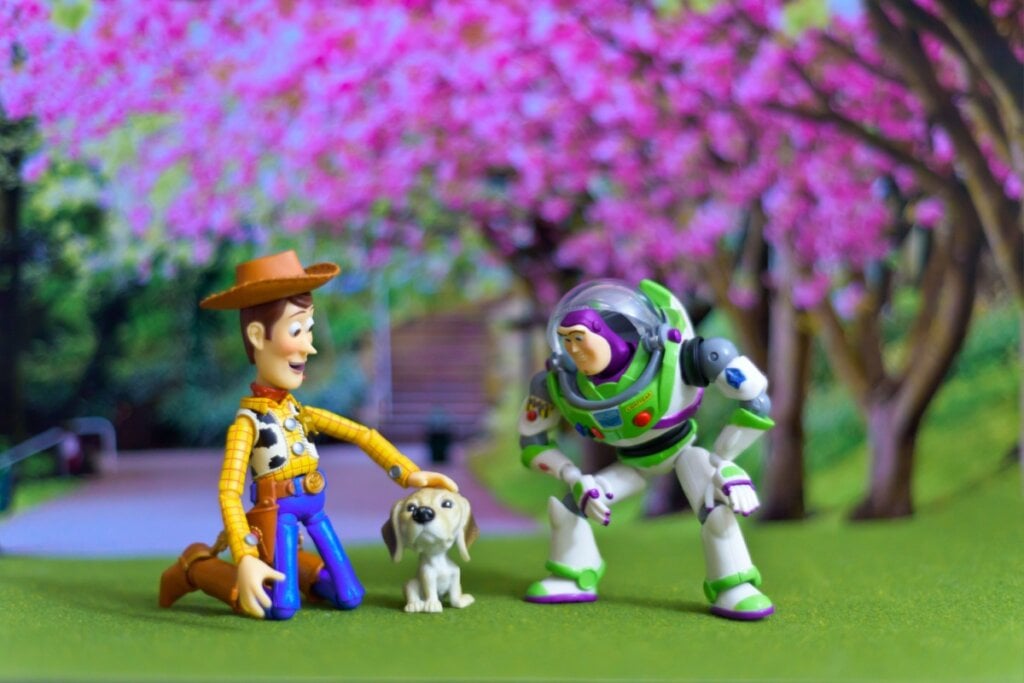 Woody, do Toy Story, ajoelhado com mão em cachorro pequeno e Buzz ao lado