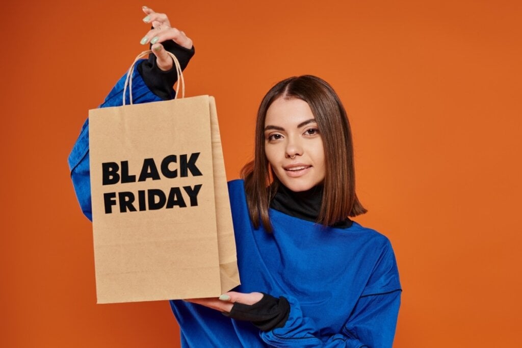 Mulher usando uma blusa azul, sorrindo e segurando uma sacola escrito "Black Friday"