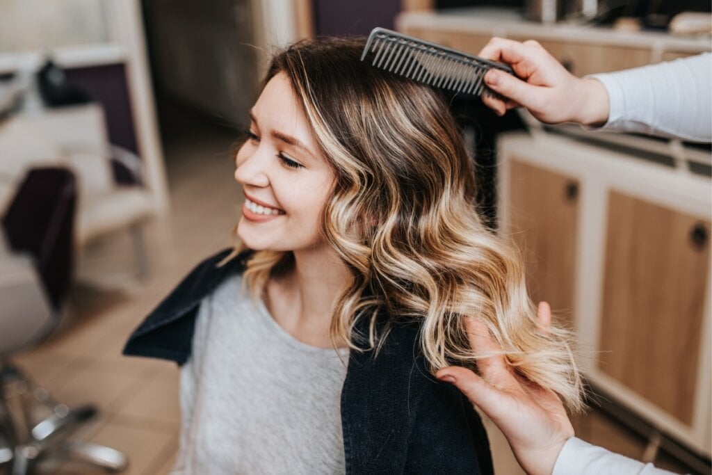 Duas mãos penteando o cabelo com mechas loiras de uma mulher sentada