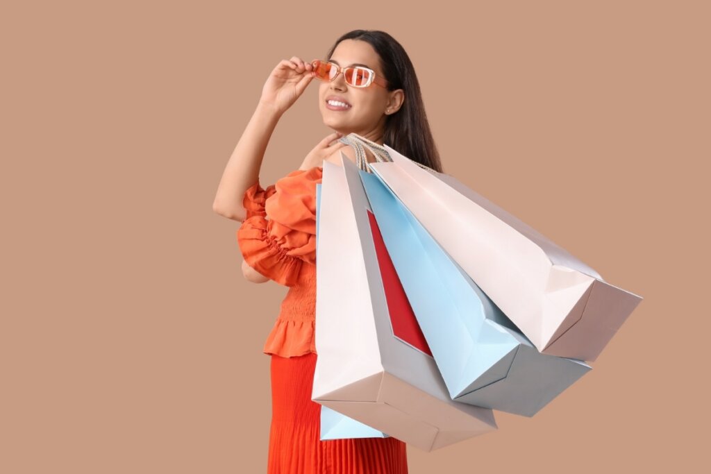 Mulher usando roupa ralada, óculos de sol e segurando sacolas de compras