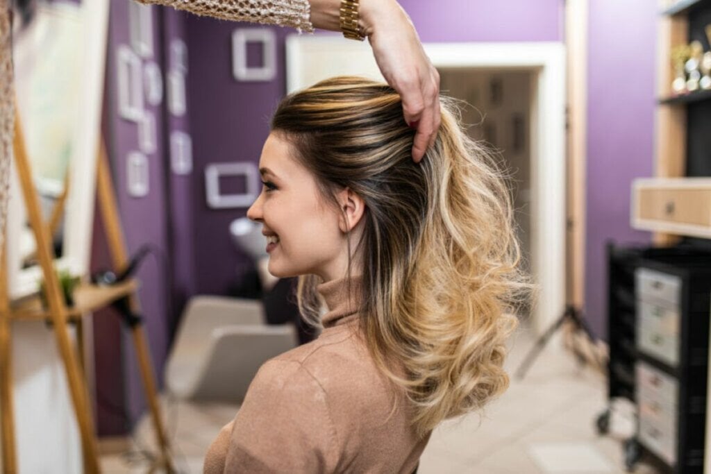 Mulher no salão com cabeleireiro mexendo em seu cabelo com luzes 