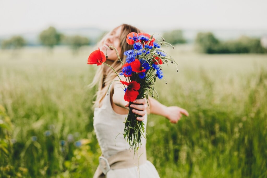 Mulher sorrindo e com os braços abertos, segurando flores em um jardim