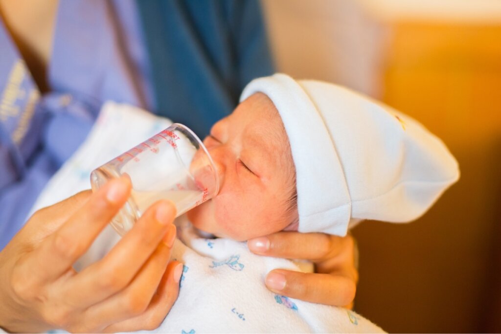 Pessoa dando leite em um copo para um bebê recém-nascido