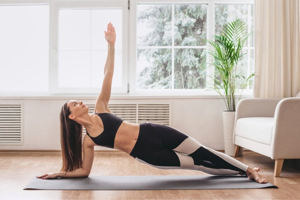 Mulher em um tapete de pilates em uma sala de estar fazendo prancha lateral