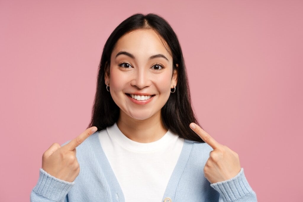 Mulher em frente a um fundo rosa sorrindo e apontando para o sorriso