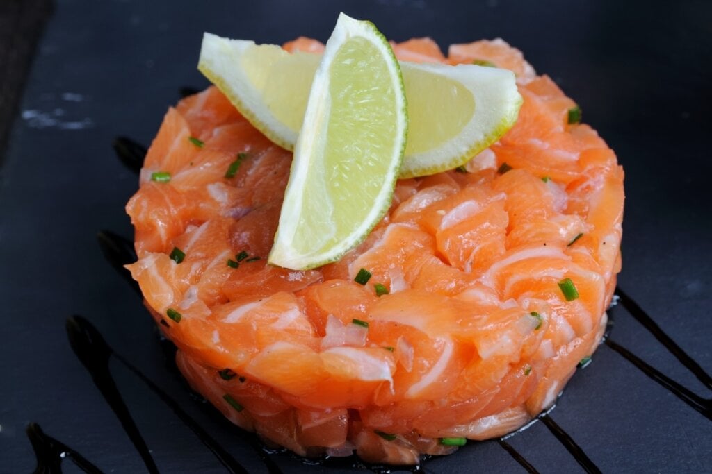 Tartare de salmão decorado com duas rodelas de limão em um fundo preto