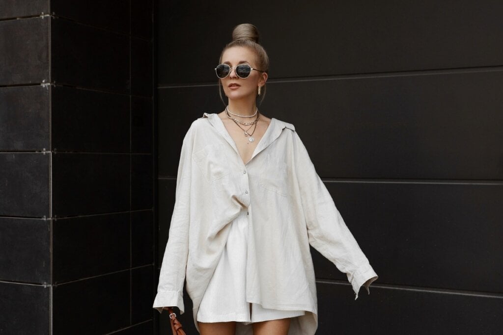 Mulher usando uma camisa de linho bege, óculos de sol preto e bermuda branca andando na rua 