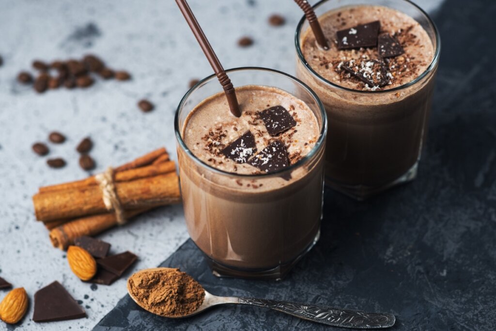 Dois copos com vitamina de chocolate em uma mesa com canela, café e chocolate